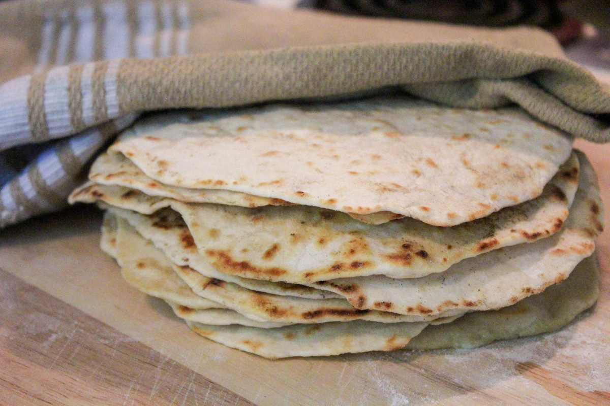 a stack of homemade flour tortillas on a wood surface