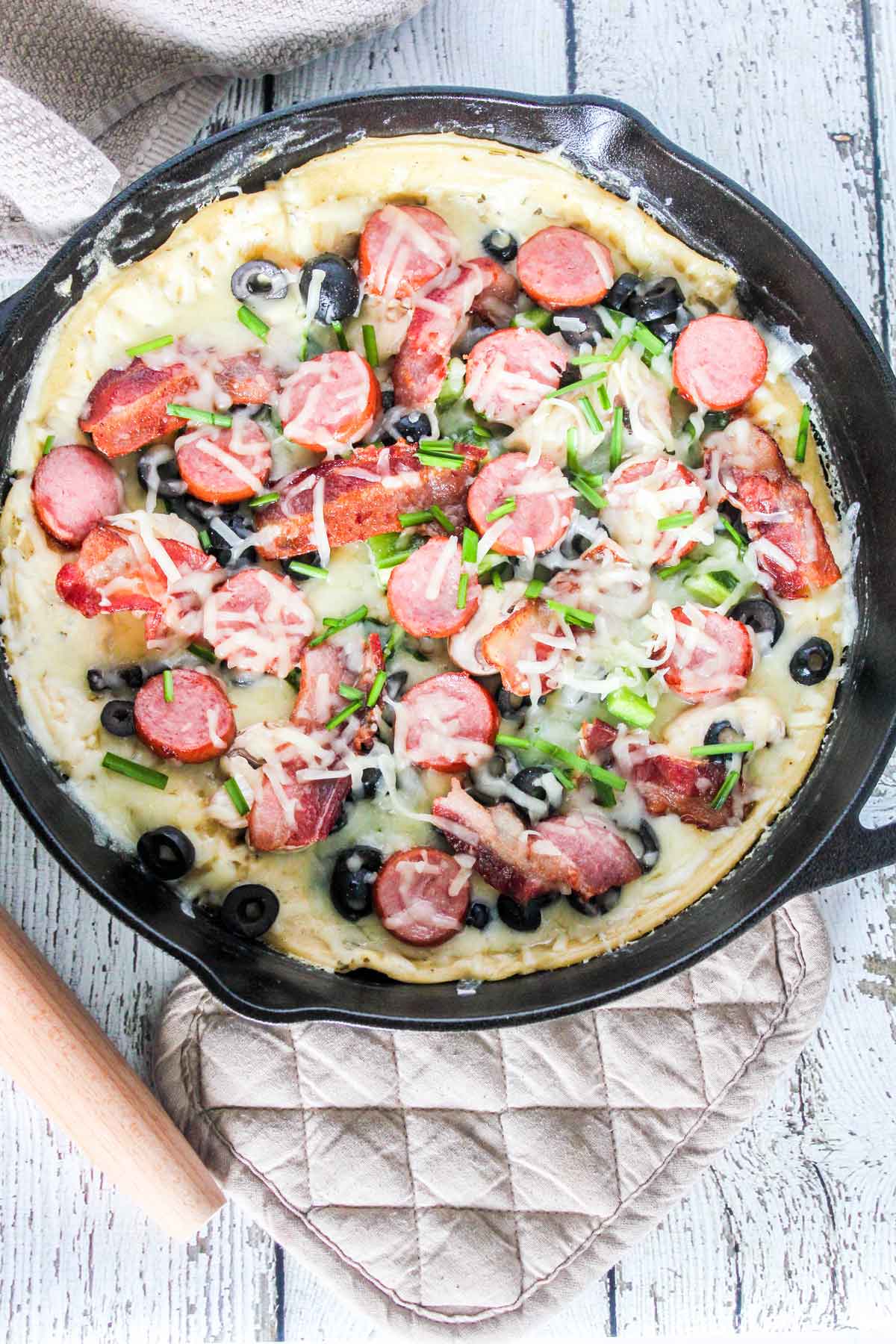 Photo of Loaded White Pesto Pizza in a skillet with a roller and pot holder