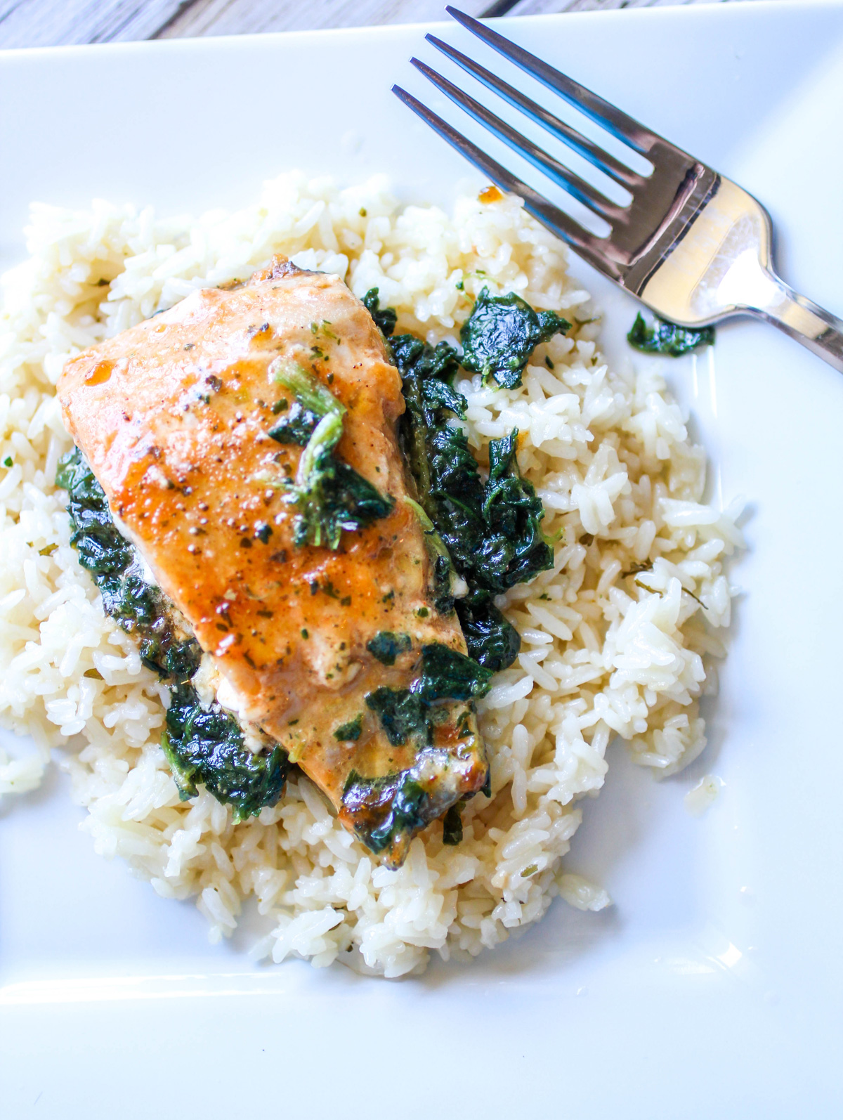 white plate with garlic butter salmon and spinach on a bed of rice